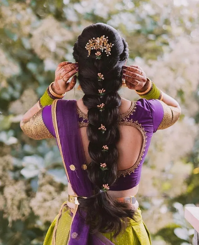 Bride’s long braid decorated with flowers and gold hair jewellery, seen from behind